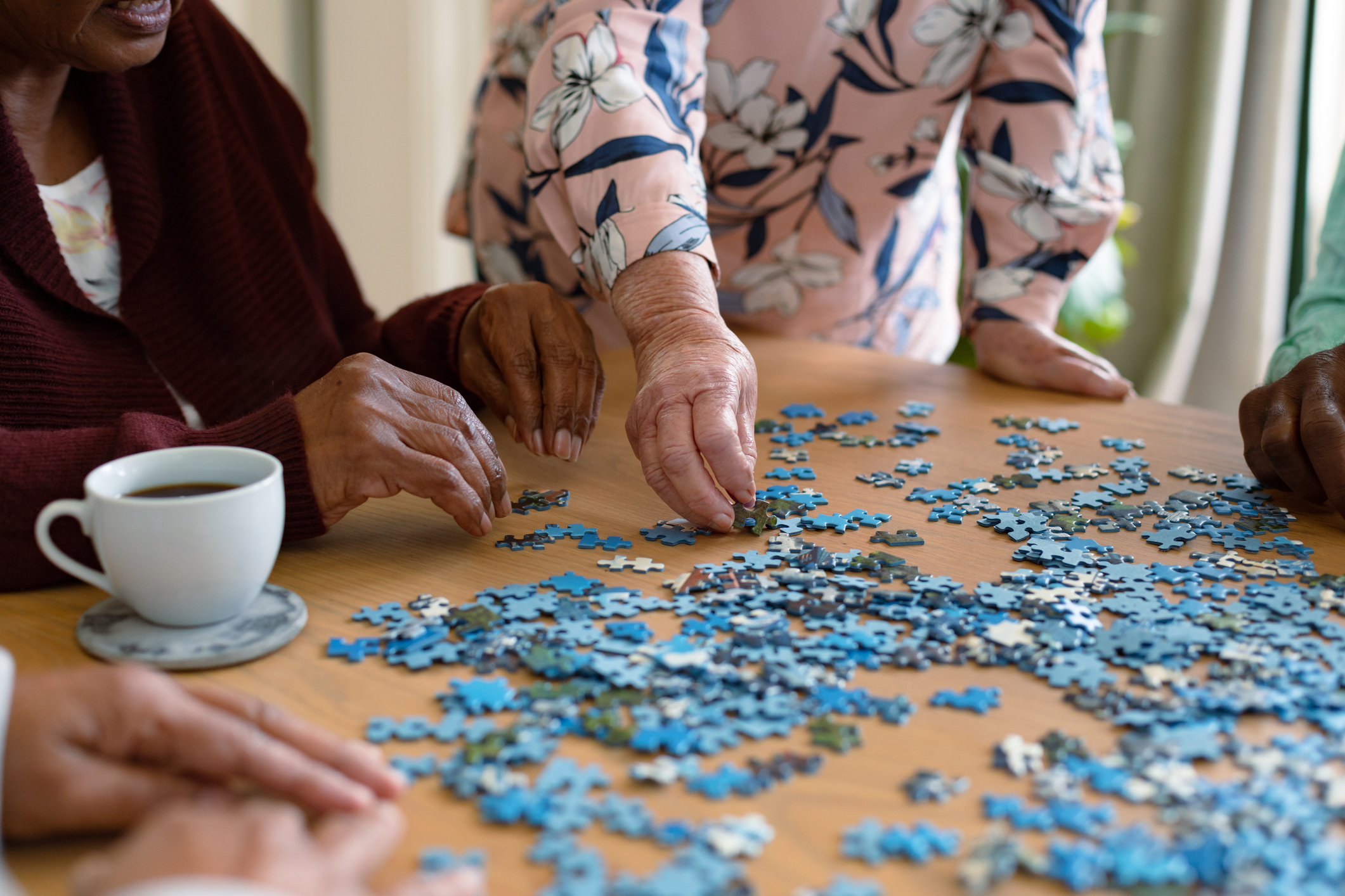 Hands of two diverse senior women and african american male friend doing puzzles. socialising with friends at home.
