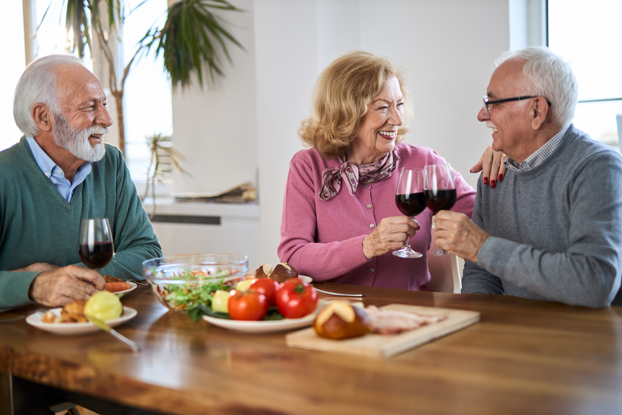Happy mature friends toasting with red wine during a meal at dining table Happy senior friends having fun while toasting with red wine during a meal at dining table