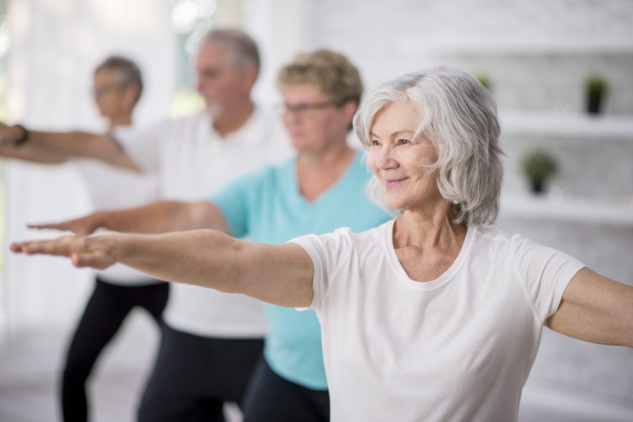 Reaching Out A multi-ethnic group of adult men and women are indoors in a fitness studio. They are wearing casual clothing while at a yoga class. A senior Caucasian woman is smiling while stretching out her arms.